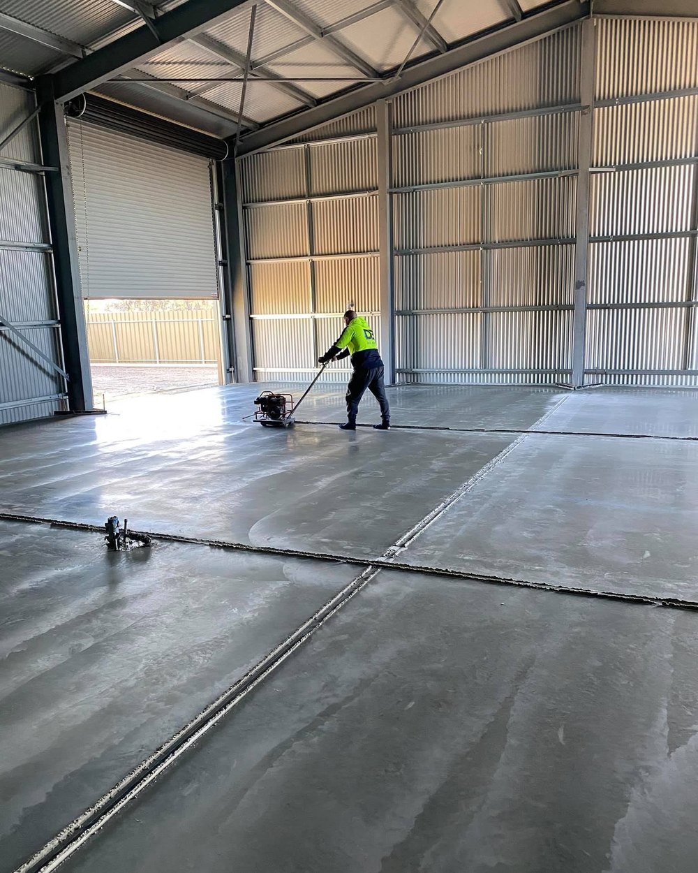 A DB Concrete crew member in branded hi-vis running a power screed over a new shed slab